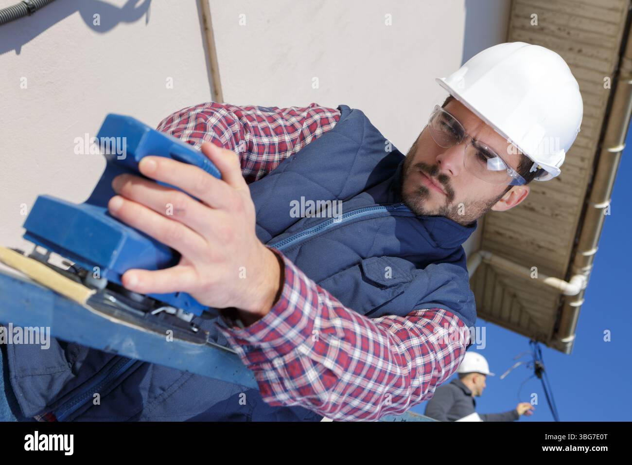 young male builder using electric sander on railing Stock Photo