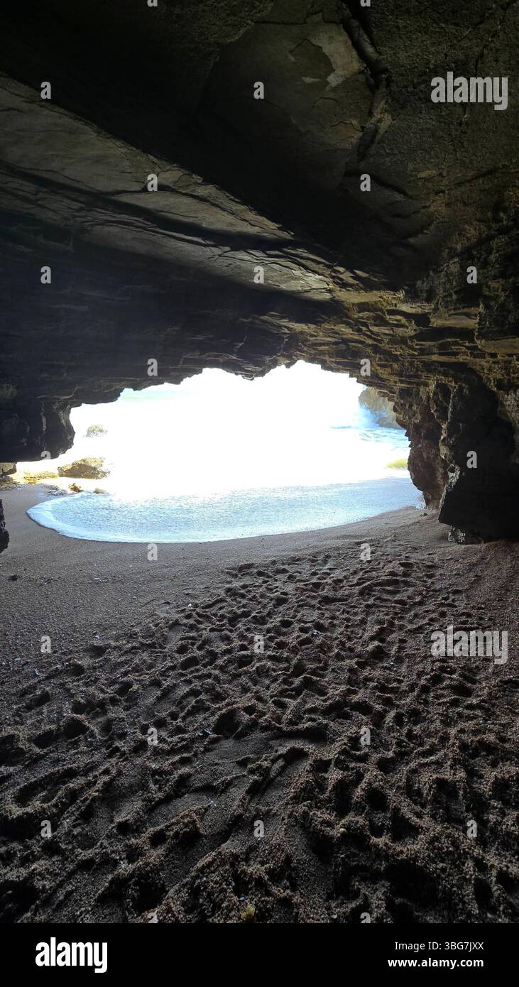 An amazing view reveals a hidden cave beach along the pristine coastline of Al Khaluf, Oman. This secluded natural wonder showcases unique rocks. - Smartphone Captured Stock Image