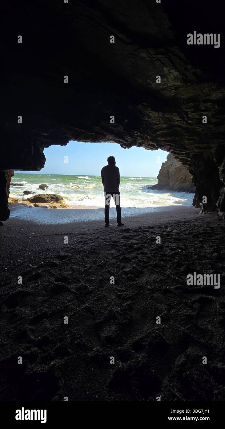 An amazing view reveals a hidden cave beach along the pristine coastline of Al Khaluf, Oman. This secluded natural wonder showcases unique rocks. - Smartphone Captured Stock Image