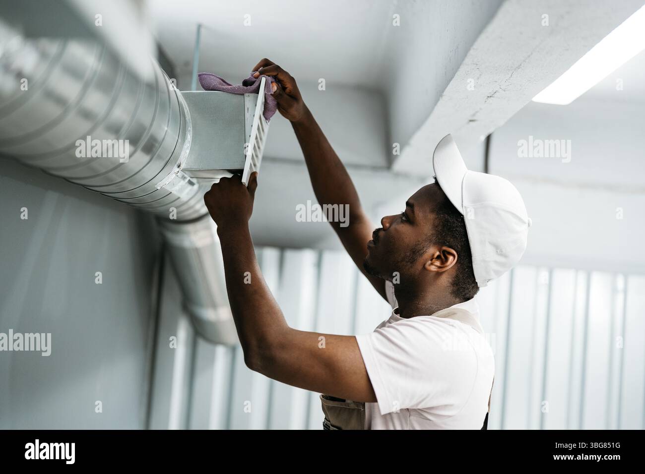 Worker performs maintenance on ventilation system in commercial building during daylight hours Stock Photo