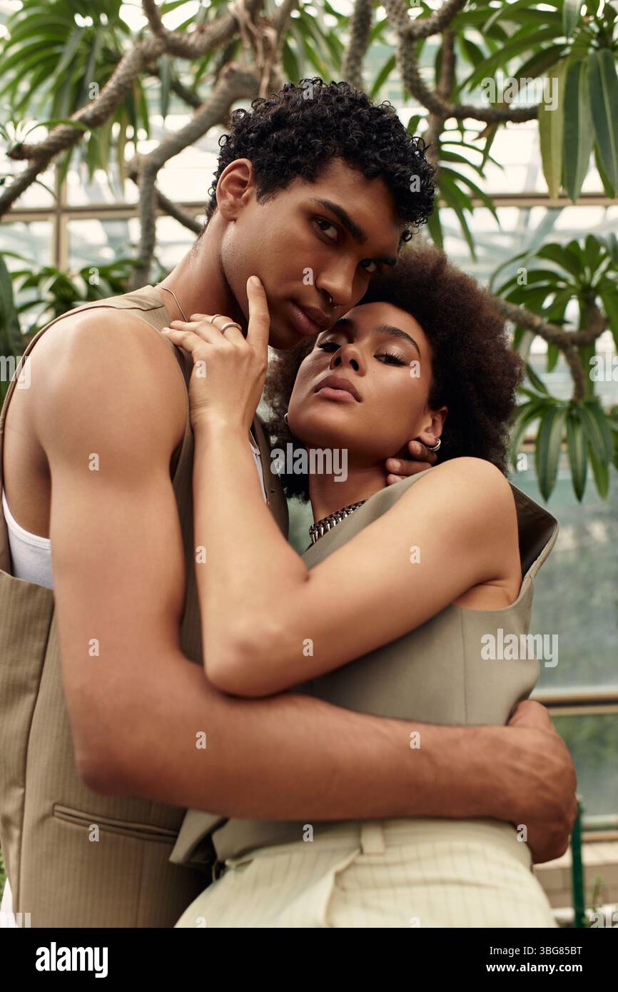 A loving couple stands close in a greenhouse filled with vibrant plants, smiling gently. Stock Photo