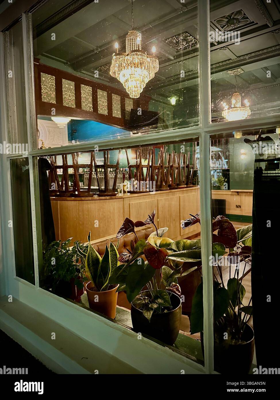 Interior of Chester Station Tap Room seen through window after closing, bar stools upturned and vintage decor lit by small chandeliers, 2 June 2025 - Smartphone Captured Stock Image