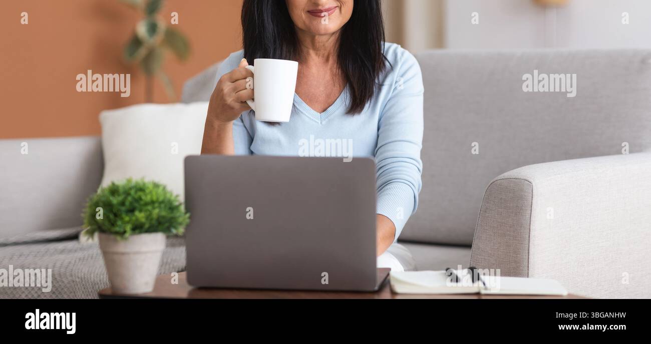 Mature woman holding coffe cup and working on computer Stock Photo