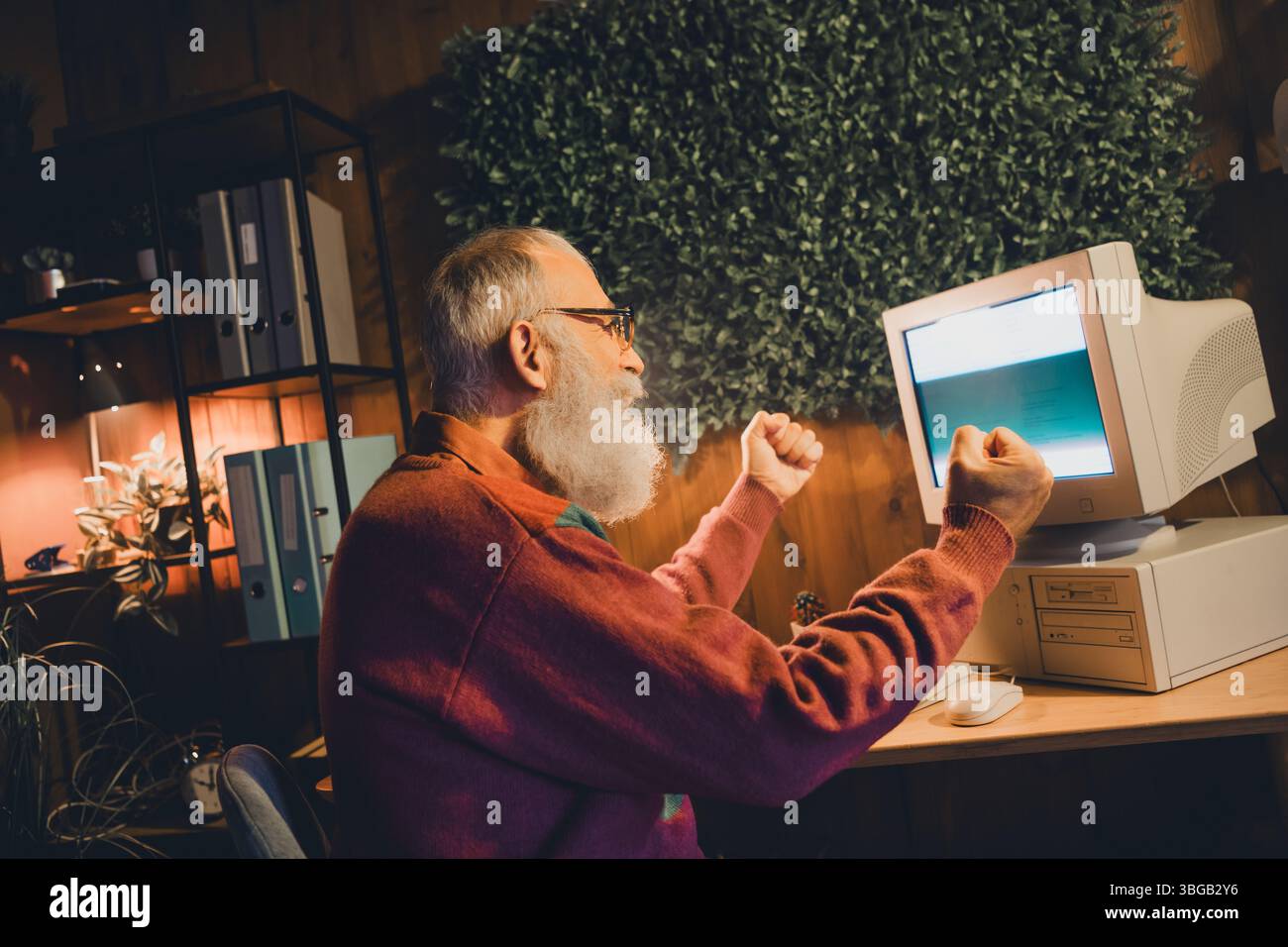 Enthusiastic elderly man engaging with technology, showcasing programming and coding skills on a vintage computer setup Stock Photo