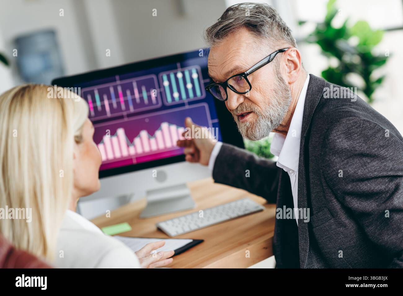 Experienced businessman discussing data with a colleague, analyzing statistics, and reviewing charts on a computer Stock Photo
