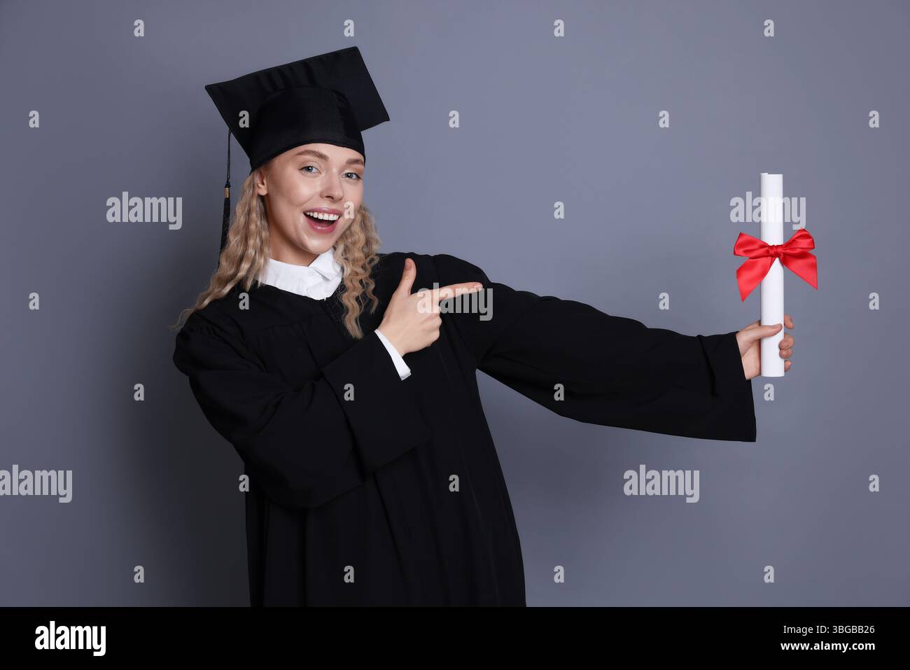 Happy student pointing at diploma after graduation on grey background ...