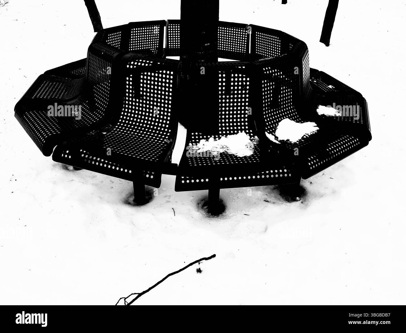 A black and white photograph shows a metal bench covered in snow. The bench has a perforated design and surrounds a central pole. - Smartphone Captured Stock Image