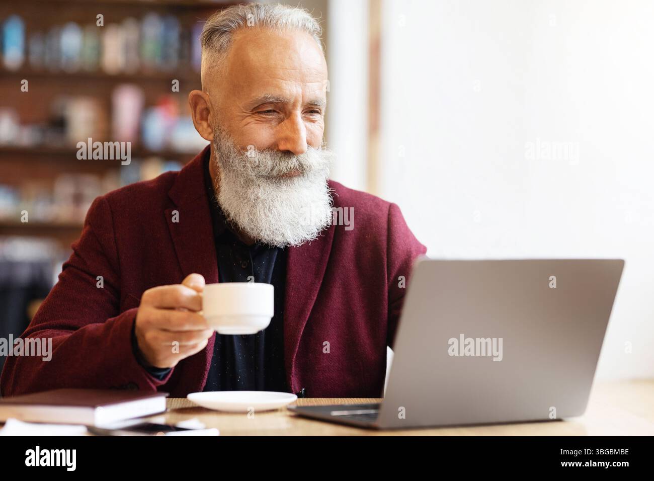 Positive senior man drinking coffee and using laptop Stock Photo