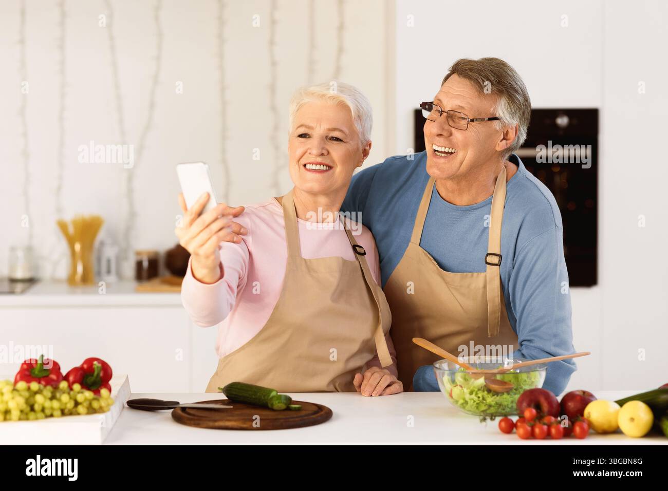 Joyful Elderly Spouses Making Selfie Having Fun Cooking In Kitchen Stock Photo