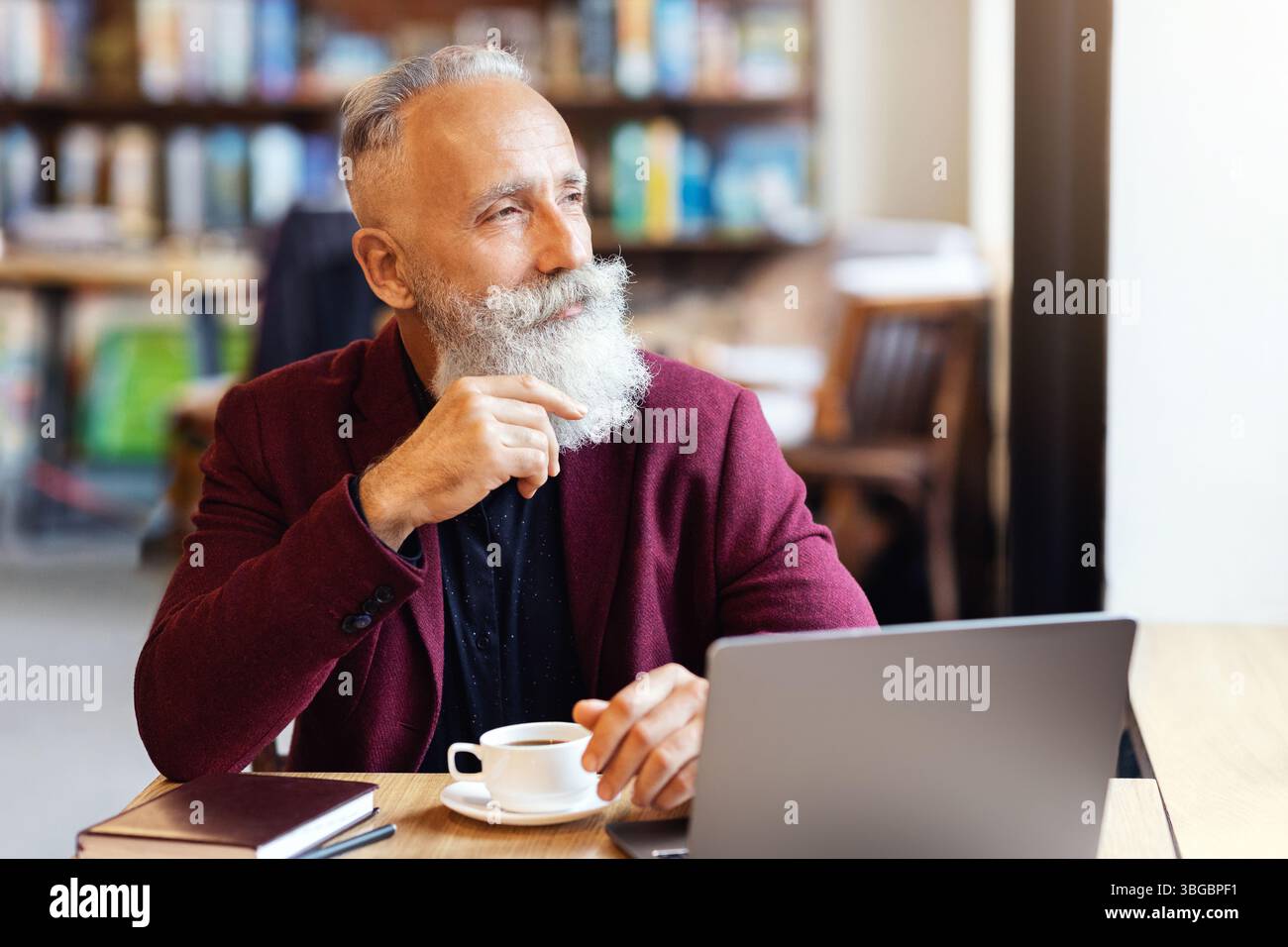 Thoughtful senior man sitting at cafe, using laptop Stock Photo