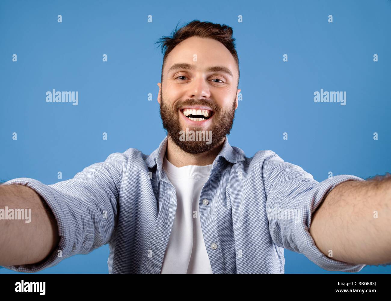 Joyful bearded guy taking selfie on blue studio background Stock Photo