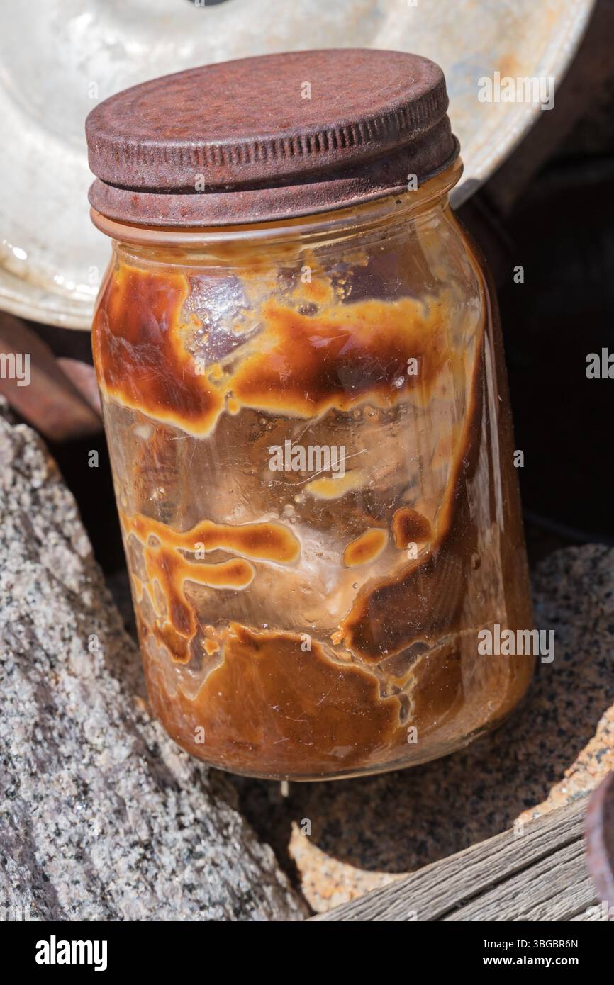 ancient discolored peanut butter in old glass jar with rusting lid in abandoned mining camp in the Inyo Mountains of California Stock Photo