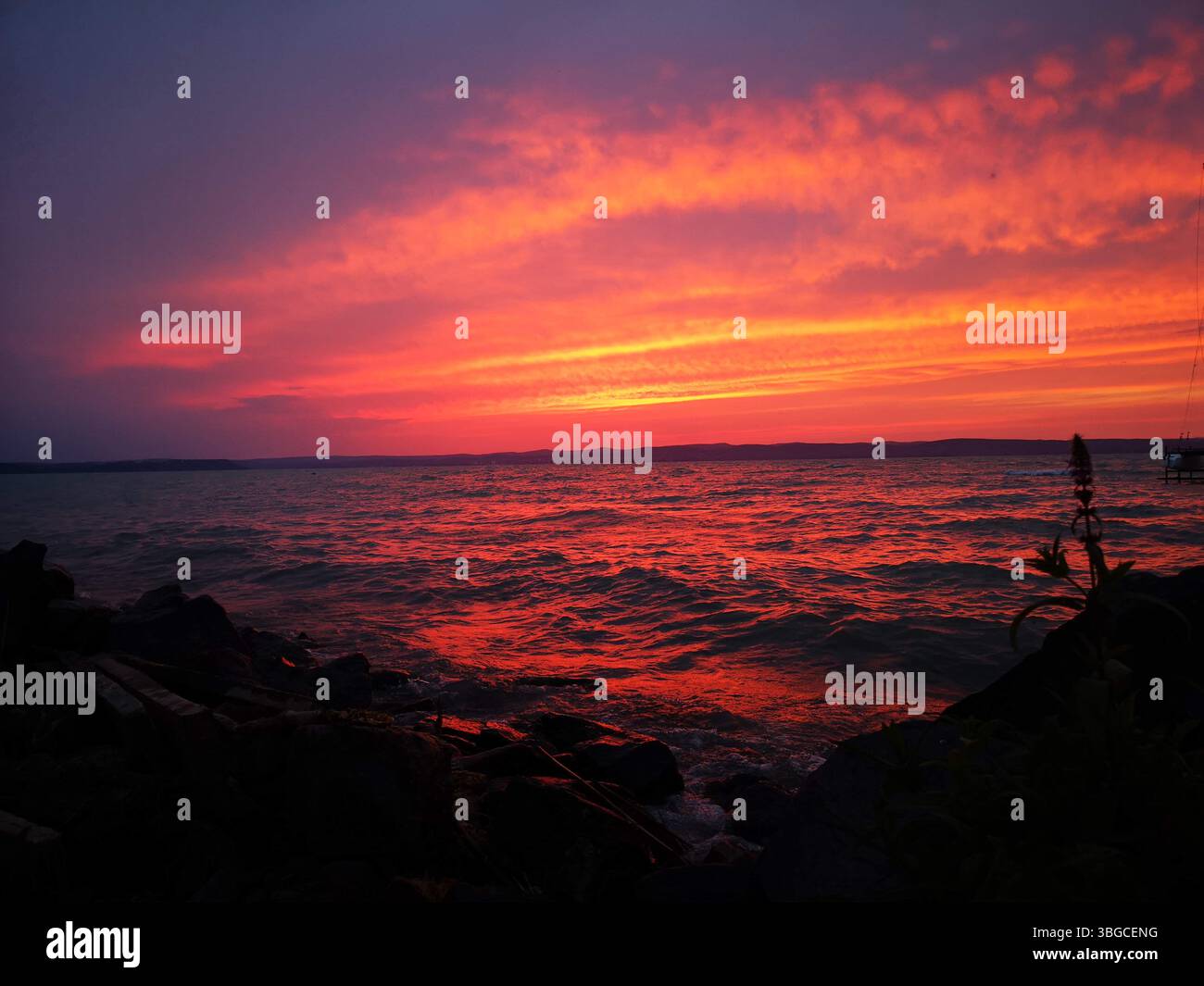 Fiery sunset over a calm coastal landscape, with dramatic orange clouds reflecting on the sea. - Smartphone Captured Stock Image