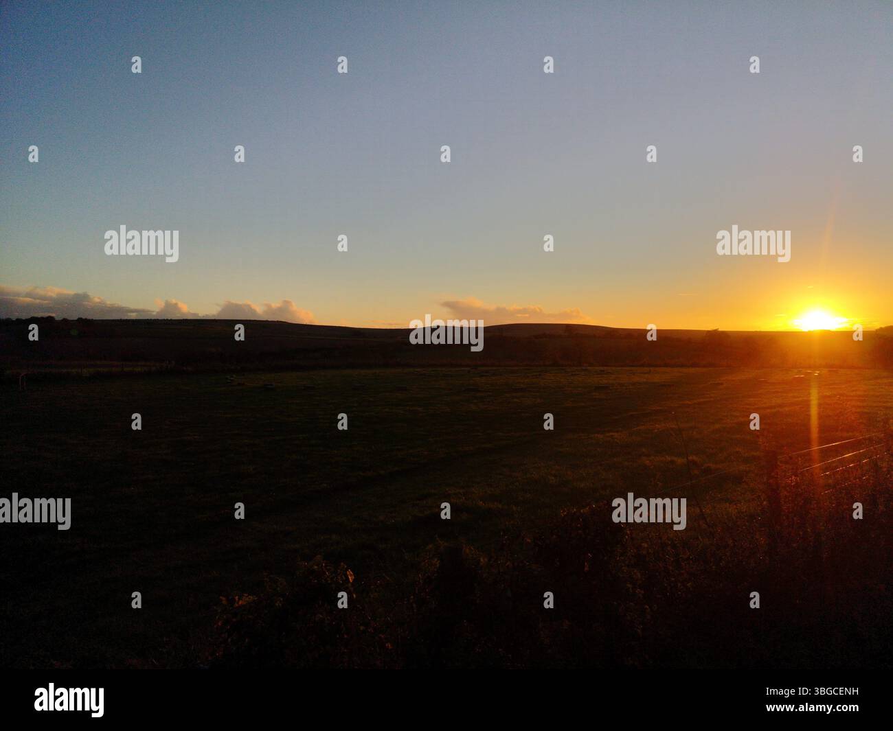 Golden sunset over rural countryside fields with soft rolling hills on the horizon. - Smartphone Captured Stock Image