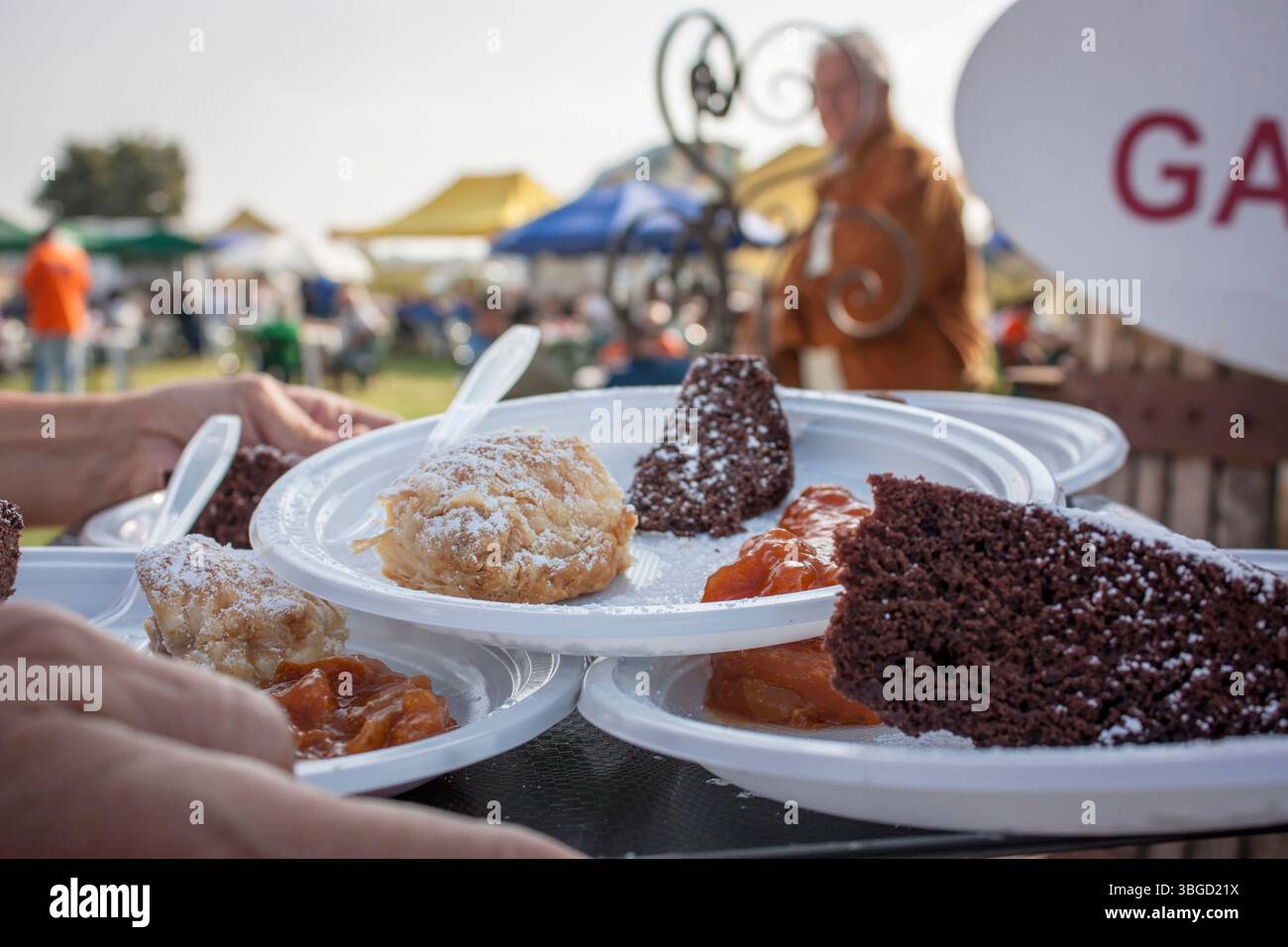 Plastic plates with various cake slices, pastries and jam being served by caterers at an outdoor event Stock Photo