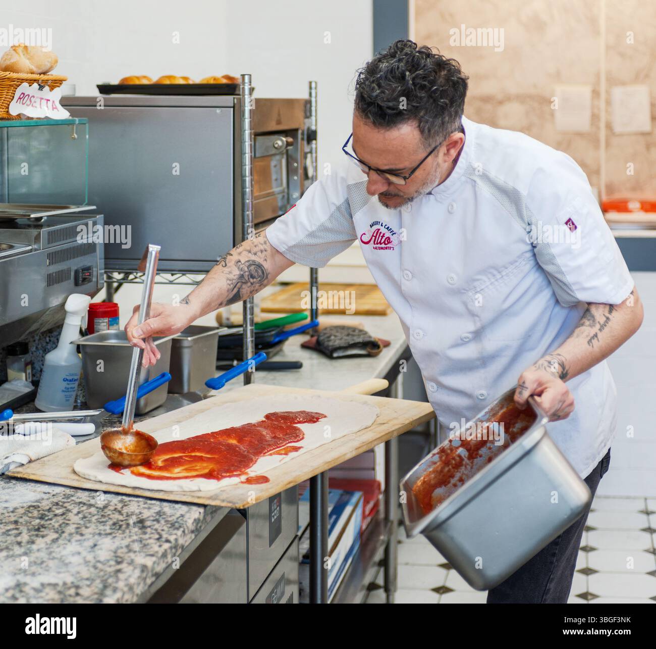 Italian Chef Preparing Artisan Pizza Dough with Tomato Sauce in a Bakery Kitchen Stock Photo