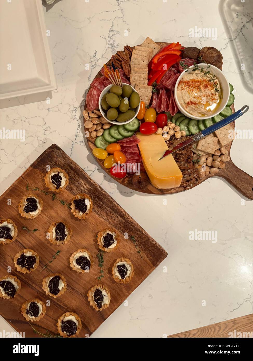 Overhead view of a charcuterie board with cured meats, cheese, olives, nuts, and tart appetizers on a marble surface. Stock Photo
