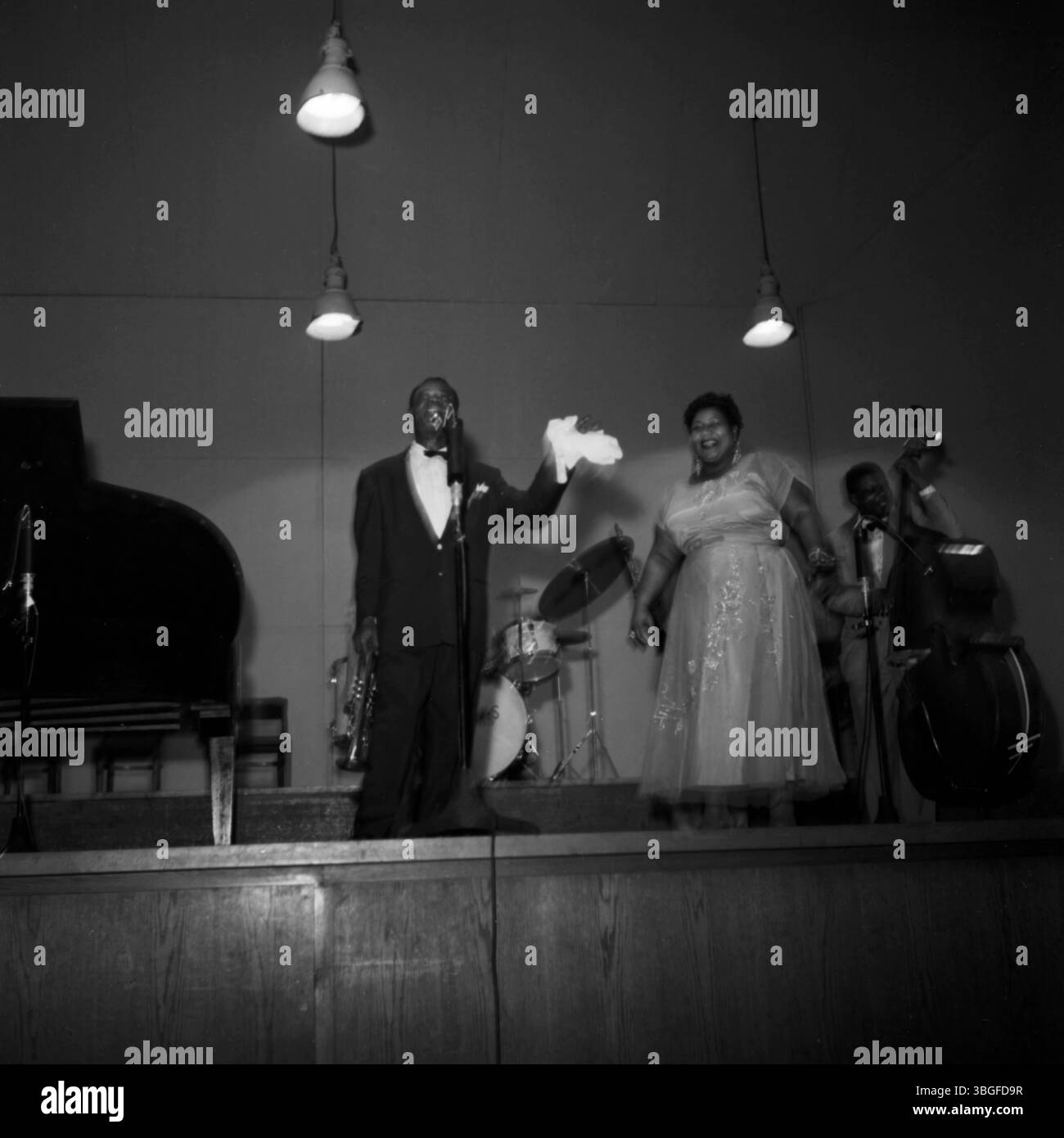 Louis Armstrong und Velma Middleton am Ende eines Konzerts in der Kongress-Halle des Deutschen Museums in München, ca. 1955. Die beiden Jazzgrößen stehen nebeneinander vor dem Mikrofon, begleitet von den All Stars. Armstrong hält sein charakteristisches Taschentuch, Ella Fitzgerald strahlt in einem eleganten Abendkleid. Stock Photo