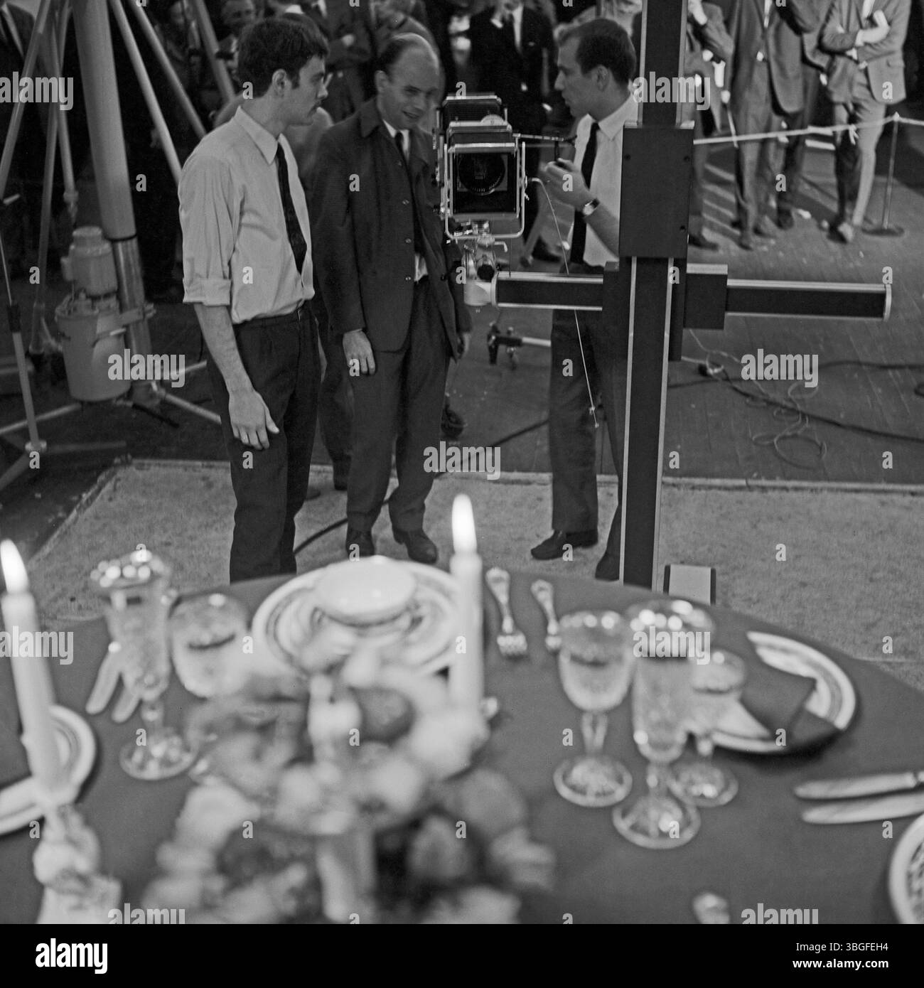 Fotografen und Techniker bei der Arbeit mit einer Sinar-Grossformat-Kamera auf der Fotokina in Köln, 1966 – im Vordergrund eine festlich gedeckte Tafel mit Kristallgläsern und Kerzen. Stock Photo