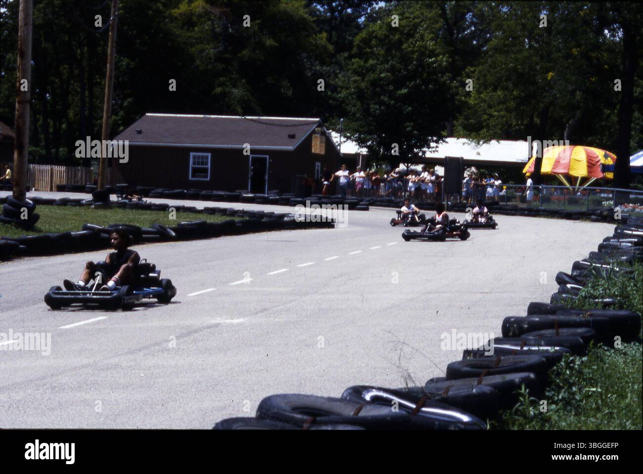 In August 1985, school-aged children enjoy a ride around a racetrack lined with tires at the Midge-o-racer attraction in Kiddie Land at Wyandot Lake Amusement Park. Spectators watch from a fenced area nearby. Stock Photo