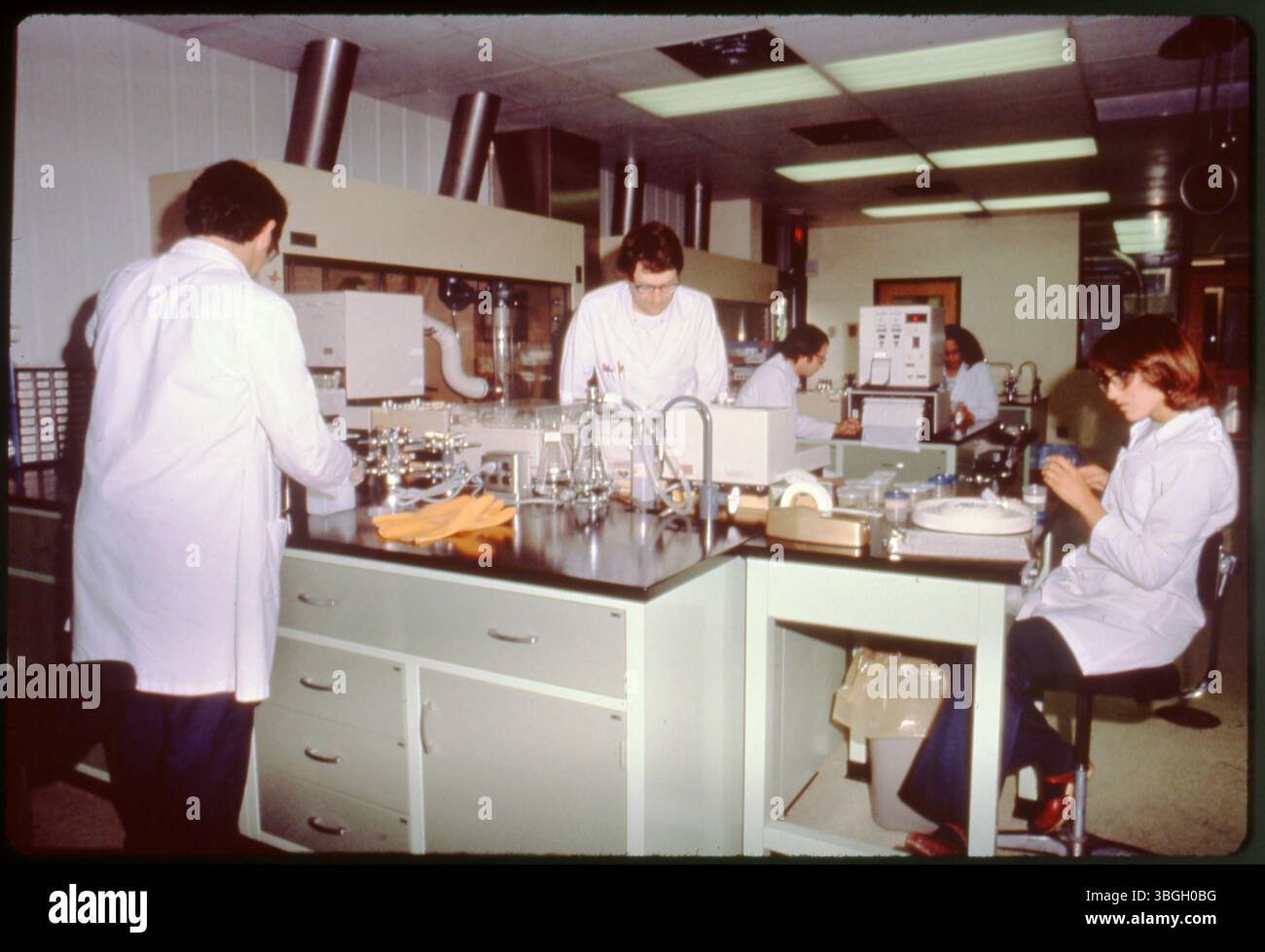 Five scientists in white lab coats are working at lab tables, handling ...