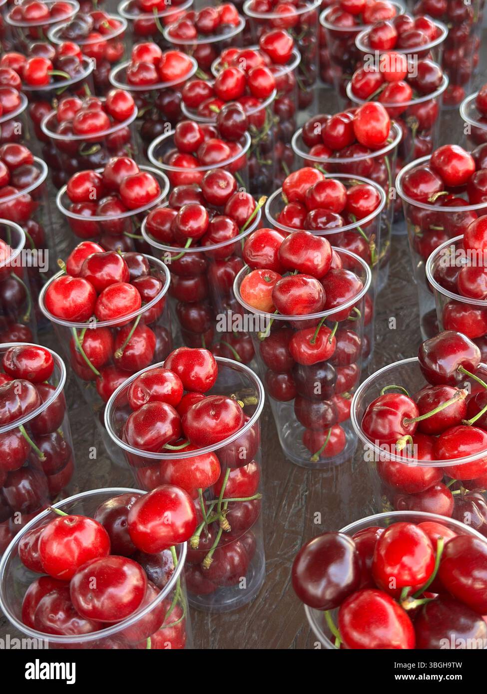 Ripe, red cherries in clear plastic cups are shown on display, ready for sale by a vendor at a food market. - Smartphone Captured Stock Image