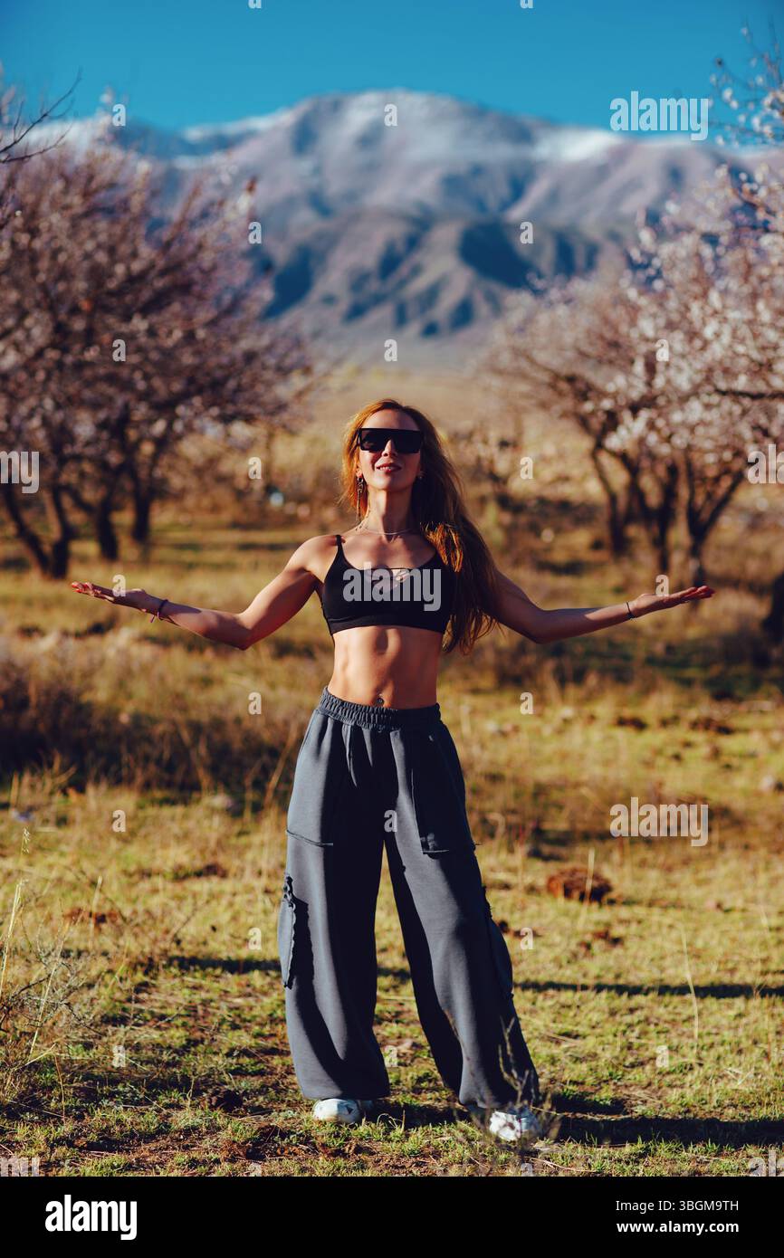 Young beautiful fitness woman posing in blooming garden on mountains background Stock Photo