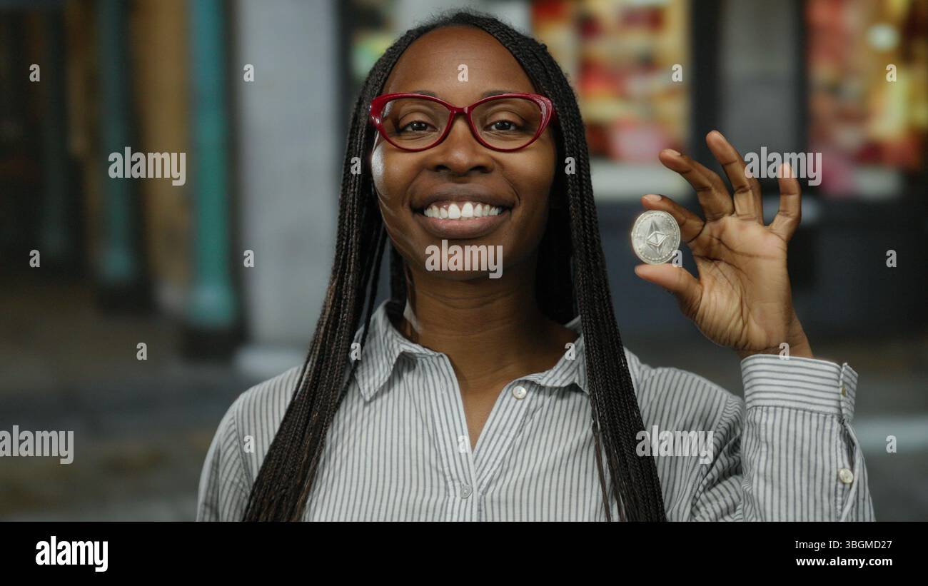Woman holding crypto coin outdoors expressing emotion in an urban street  setting, emphasizing virtual currency impact on african american lifestyle  an Stock Photo - Alamy