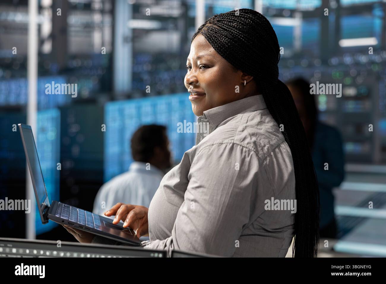 Smiling technician in server room using laptop to implement and manage data backup solutions. Happy data center engineer identifying and resolving technical issues, ensuring efficient recovery Stock Photo