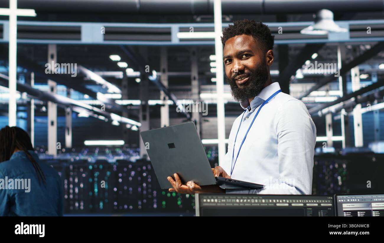 Happy data center admin uses node tree programming on laptop to identify equipment performance issues. Cheerful server farm worker reviews data analysis graph to minimize hardware failures, camera B Stock Photo