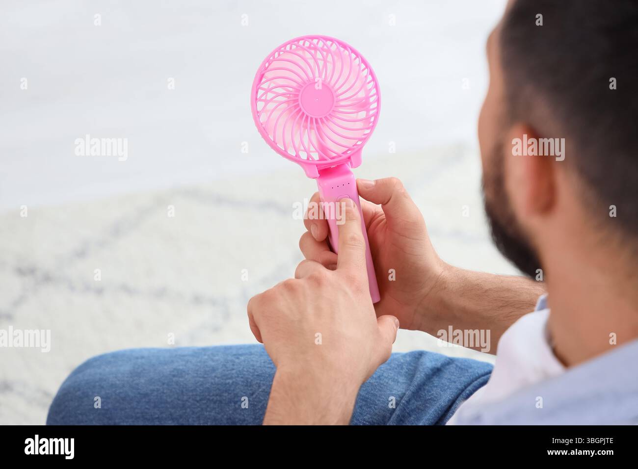 Young man turning on mini fan at home, closeup Stock Photo - Alamy