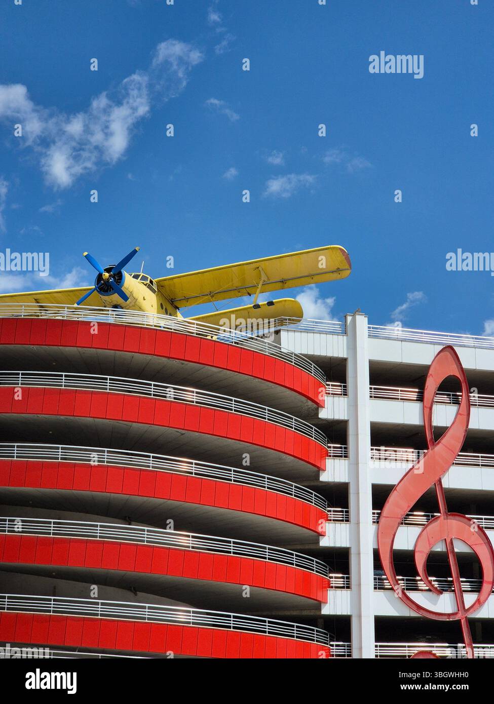 A biplane, multi-storey car park and large treble clef symbol under blue sky - Smartphone Captured Stock Image