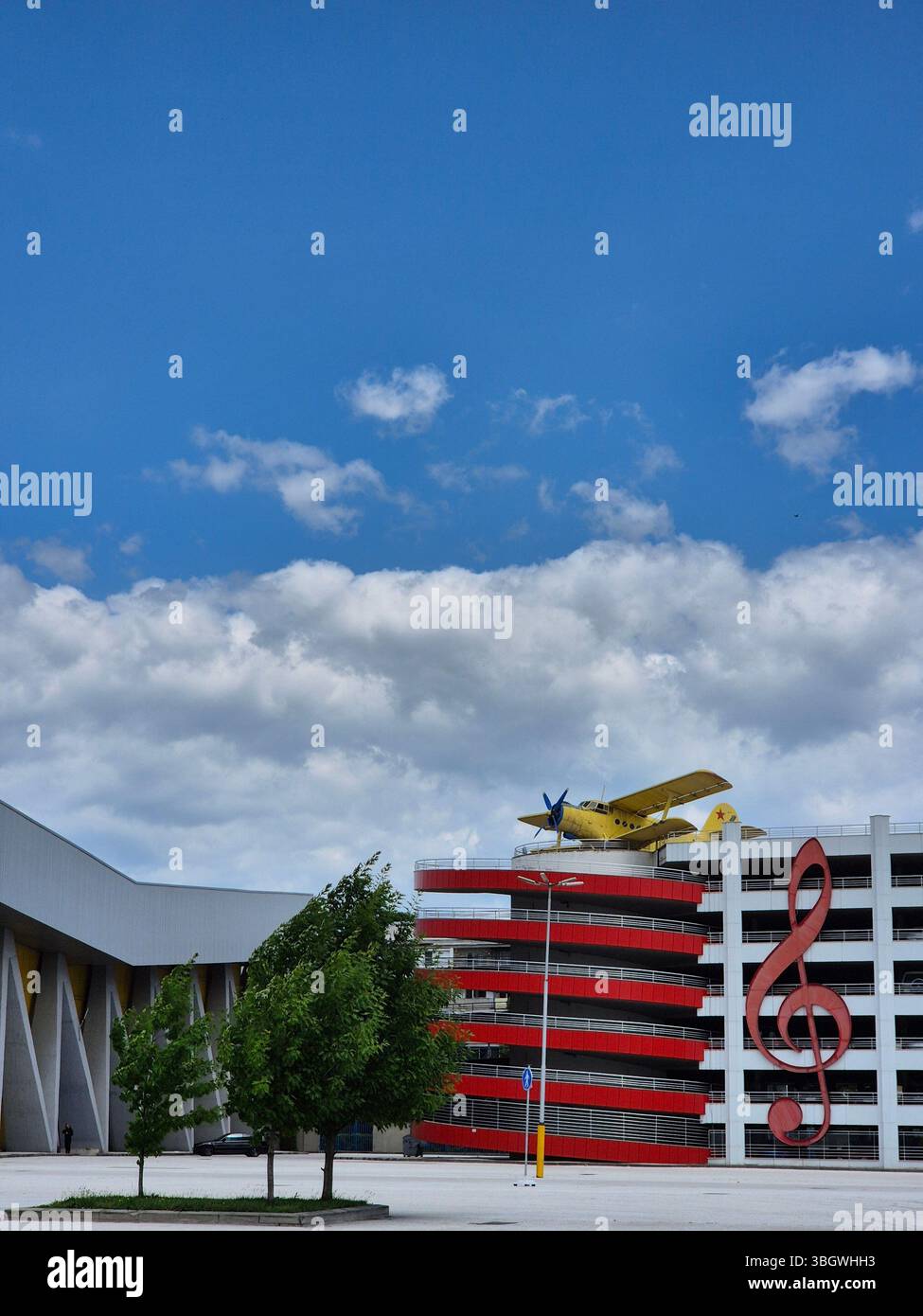 A biplane, multi-storey car park and large treble clef symbol under blue sky - Smartphone Captured Stock Image