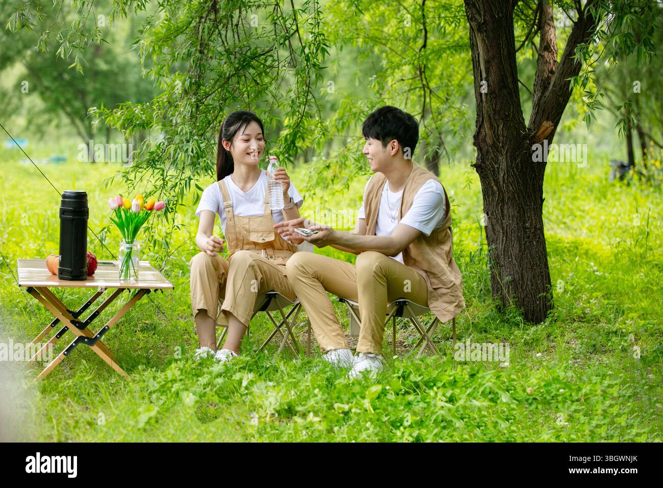 a young couple resting under a big tree while using their phones Stock Photo