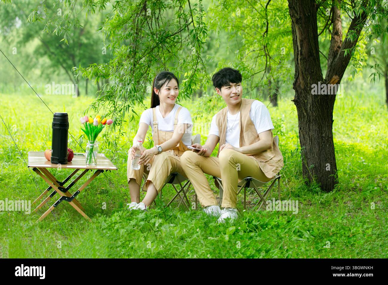 a young couple resting under a big tree while using their phones Stock Photo