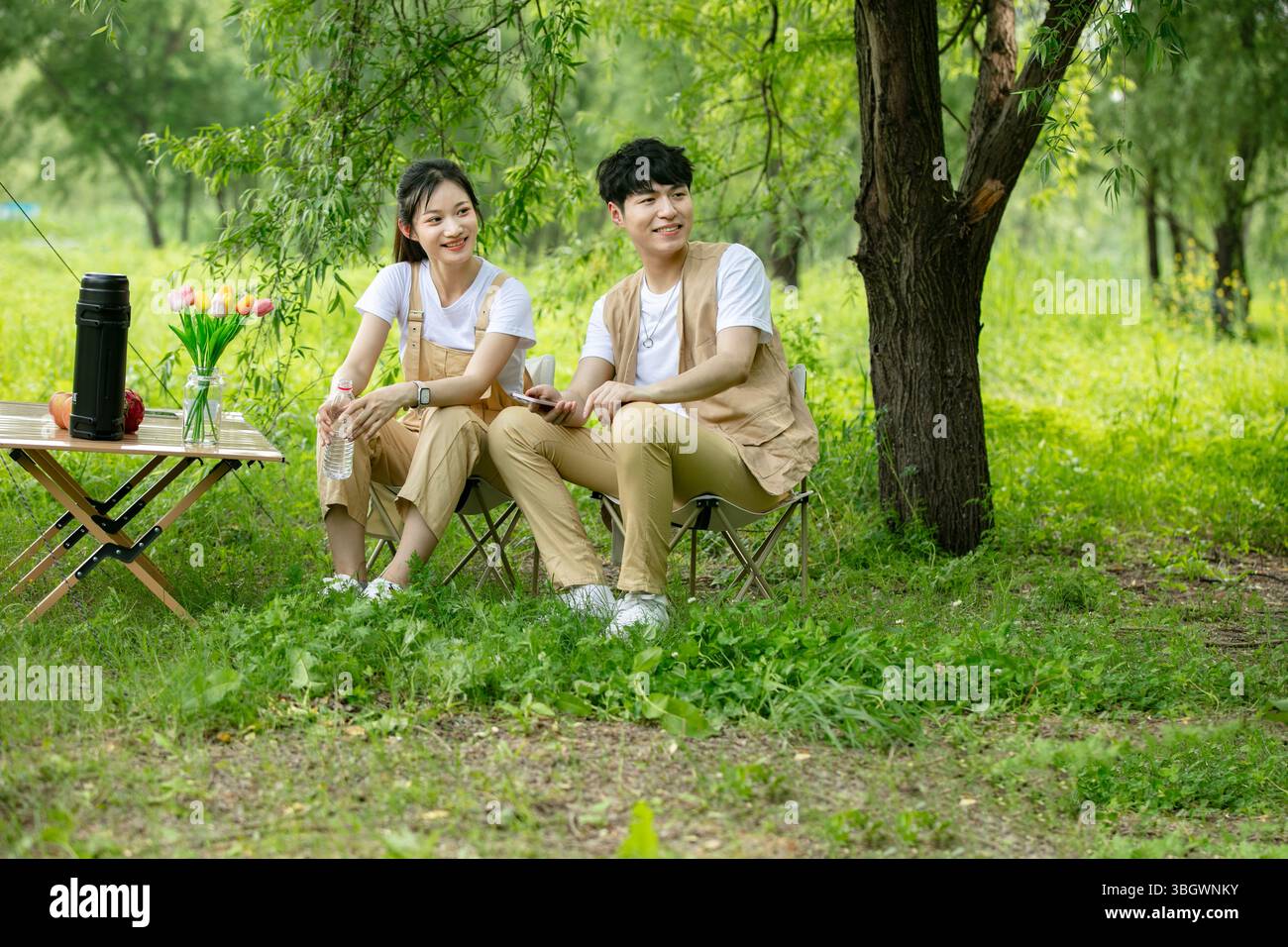 a young couple resting under a big tree while using their phones Stock Photo