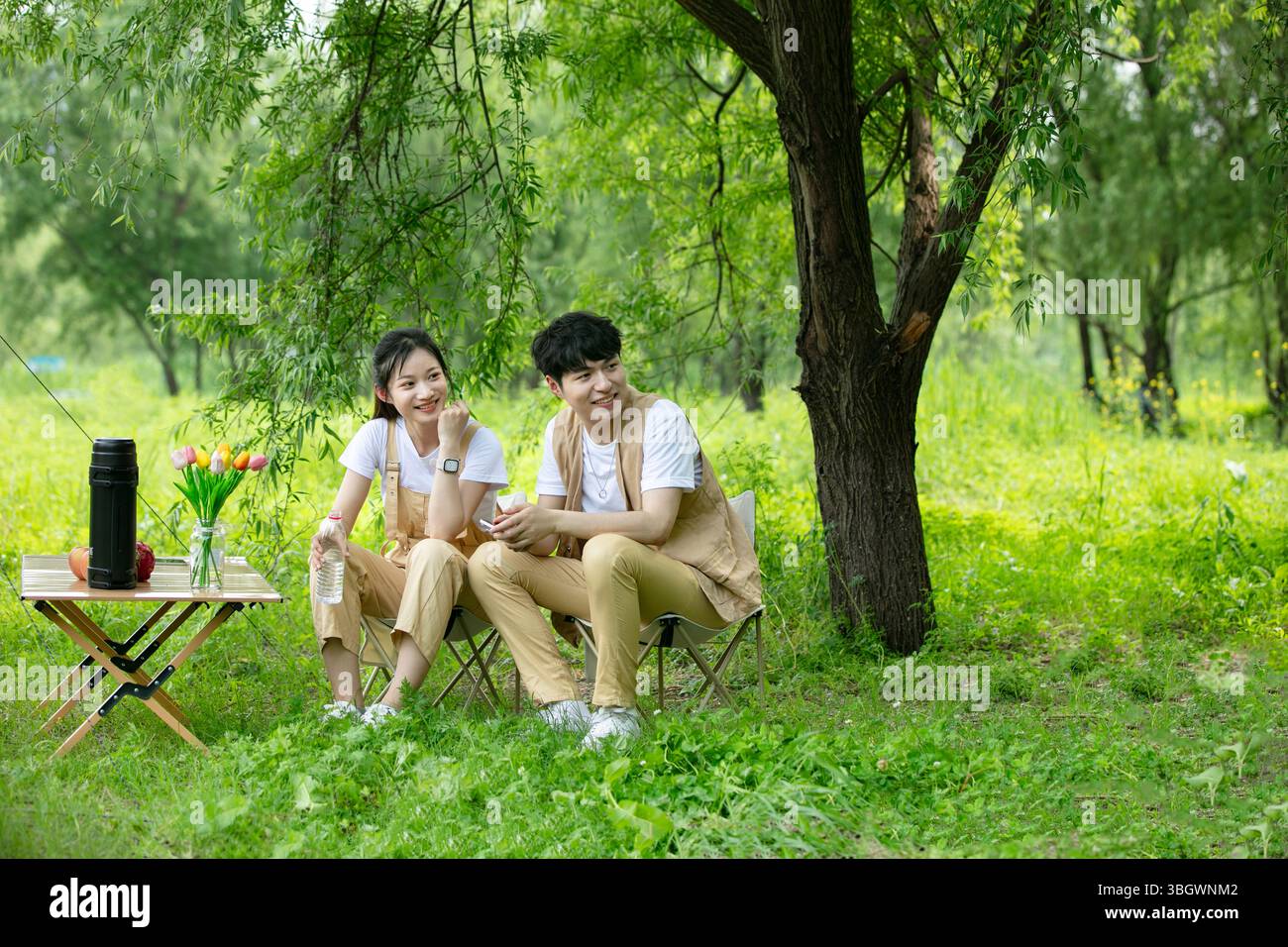 a young couple resting under a big tree while using their phones Stock Photo