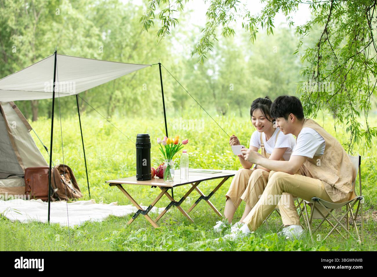 a young couple resting under a big tree while using their phones Stock Photo