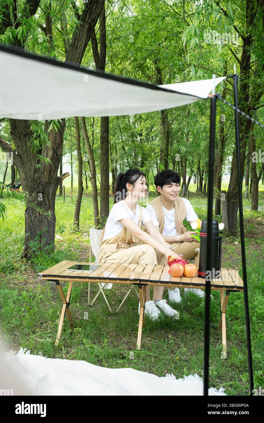 a young couple resting under a big tree while using their phones Stock Photo