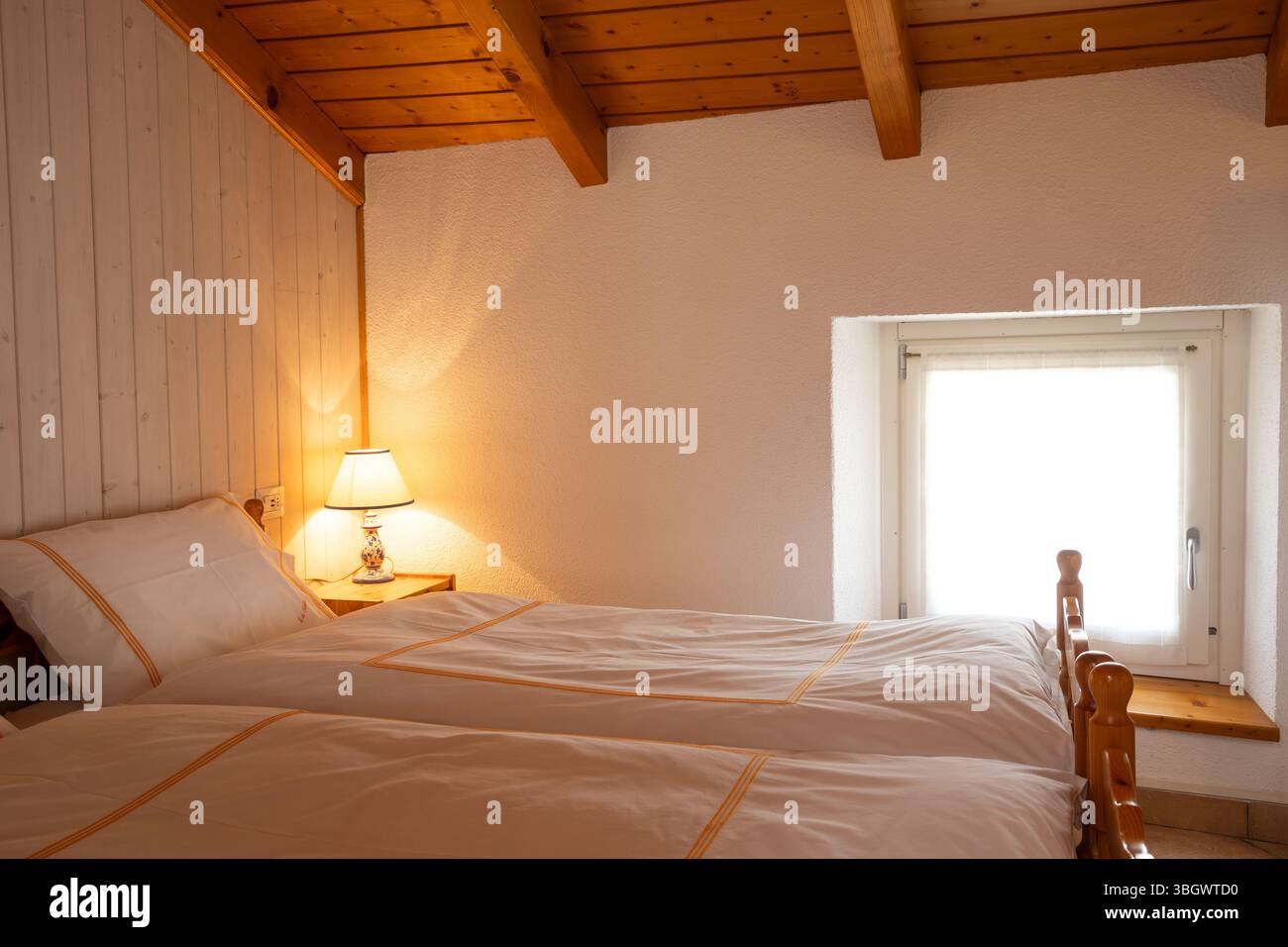 Interior of a double bedroom with two beds in a mountain hut. A bright light warms the room and makes it very cosy Stock Photo