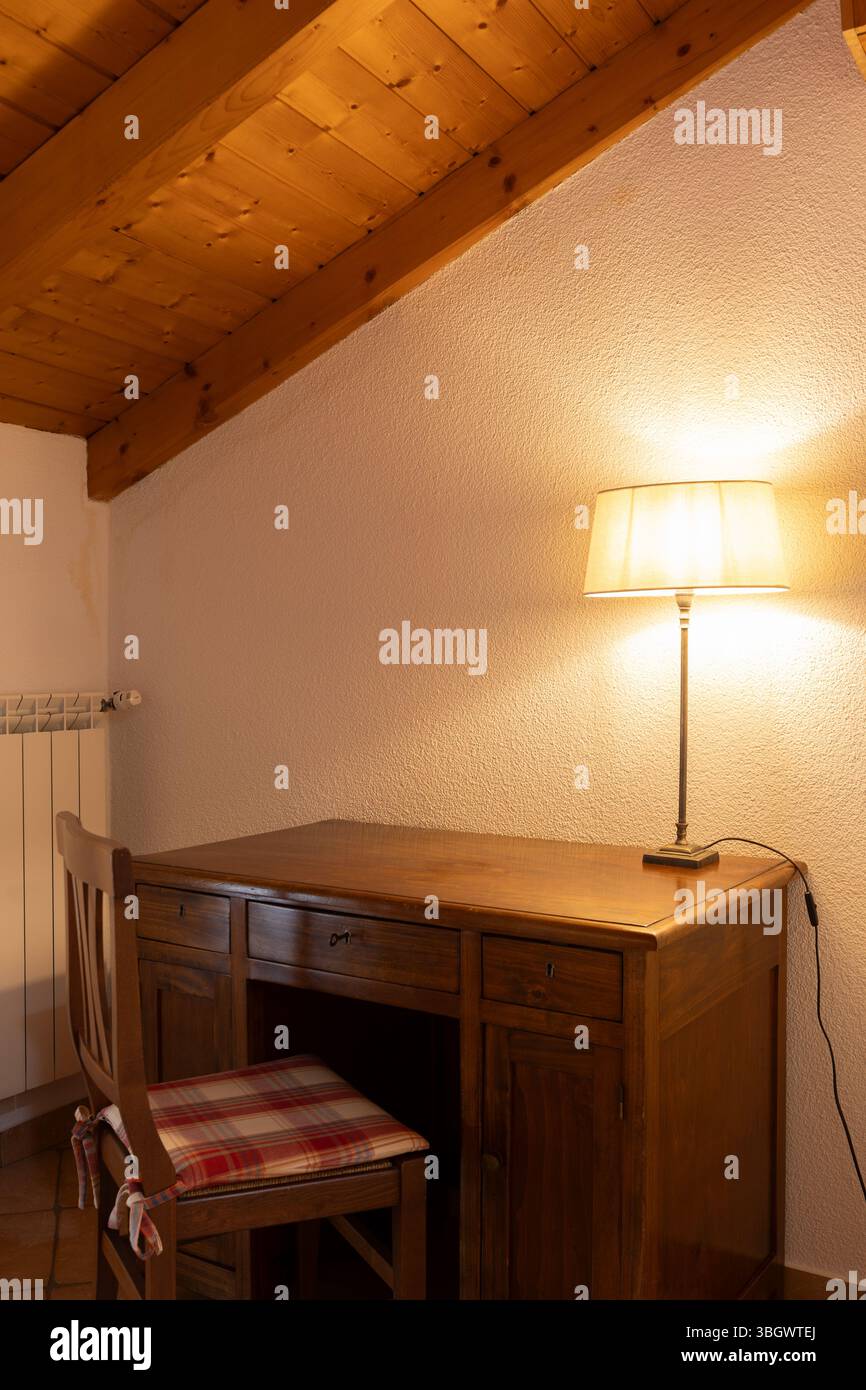 Detail of a corner of a bedroom with a desk a chair and a lamp with a light on Stock Photo