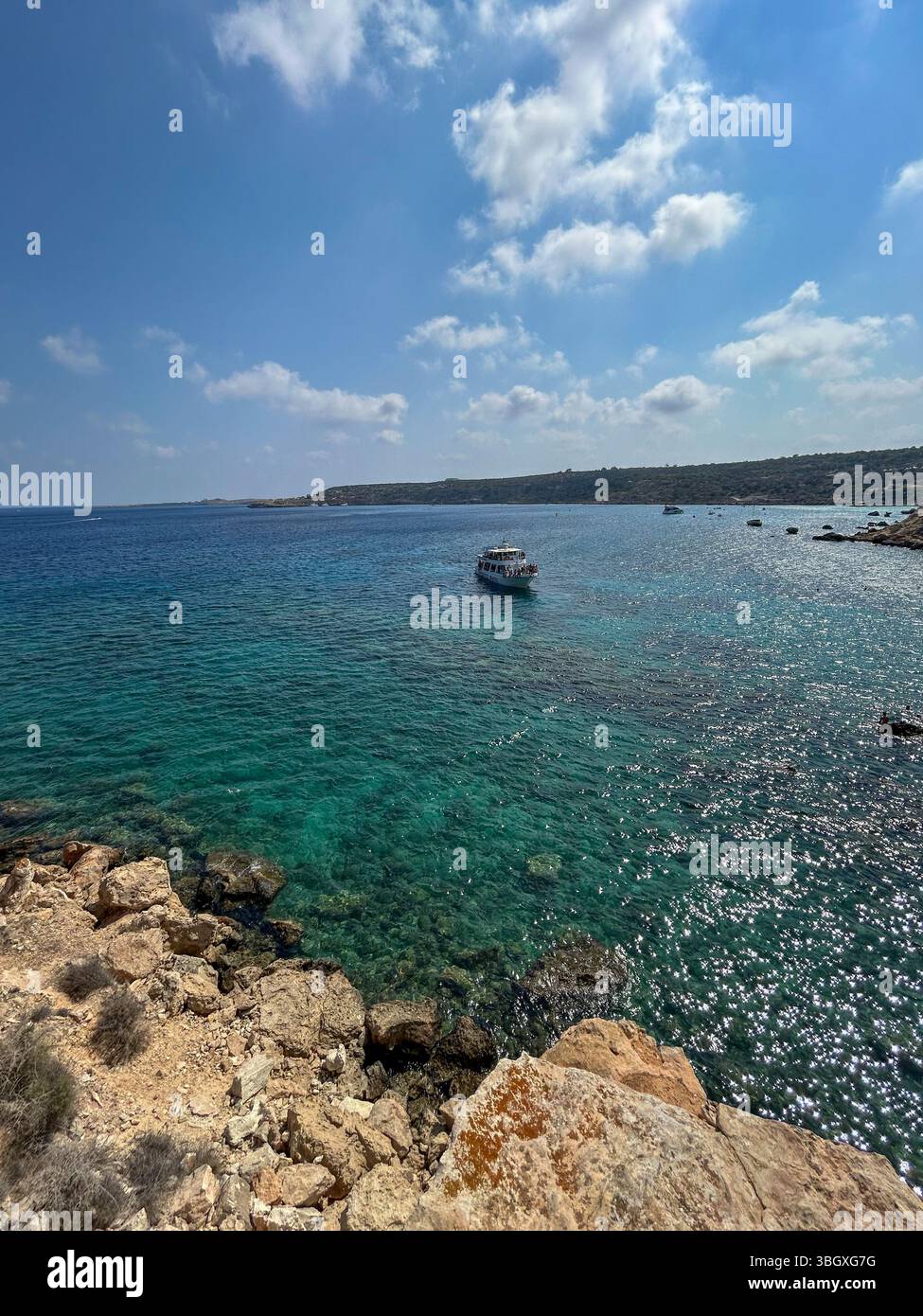 Tour boat floating on sparkling turquoise sea near rocky coastline under a sunny sky, capturing a peaceful Mediterranean summer scene. - Smartphone Captured Stock Image