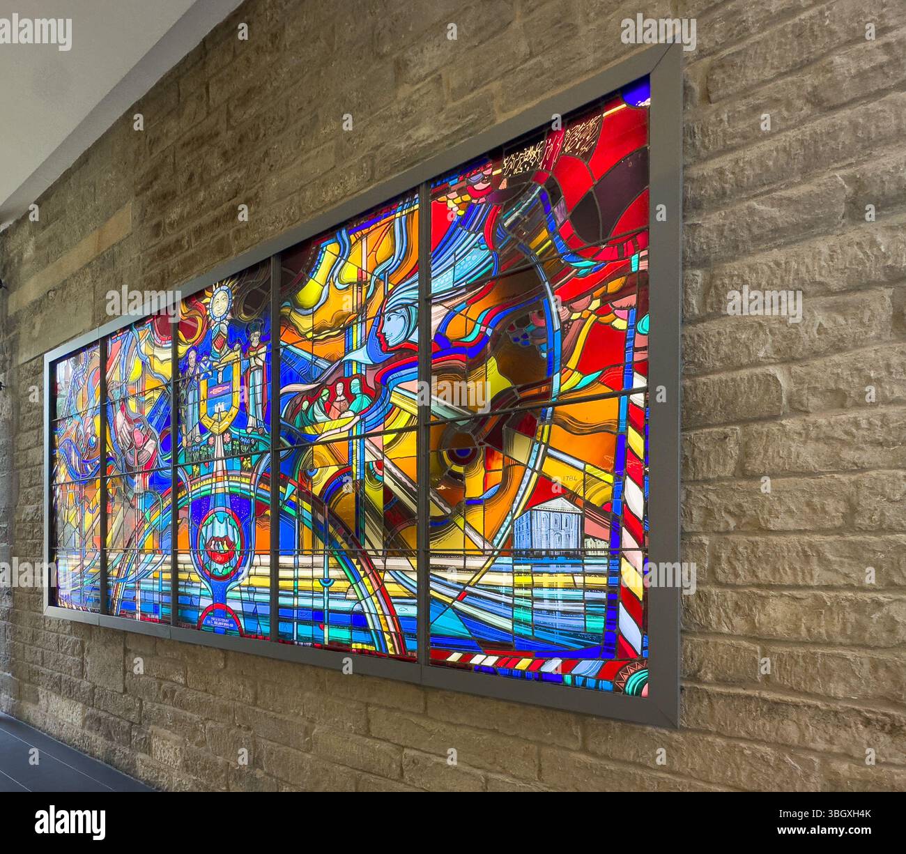 Vibrant modern stained glass panel artwork mounted on a textured brick wall in a well-lit indoor space Stock Photo