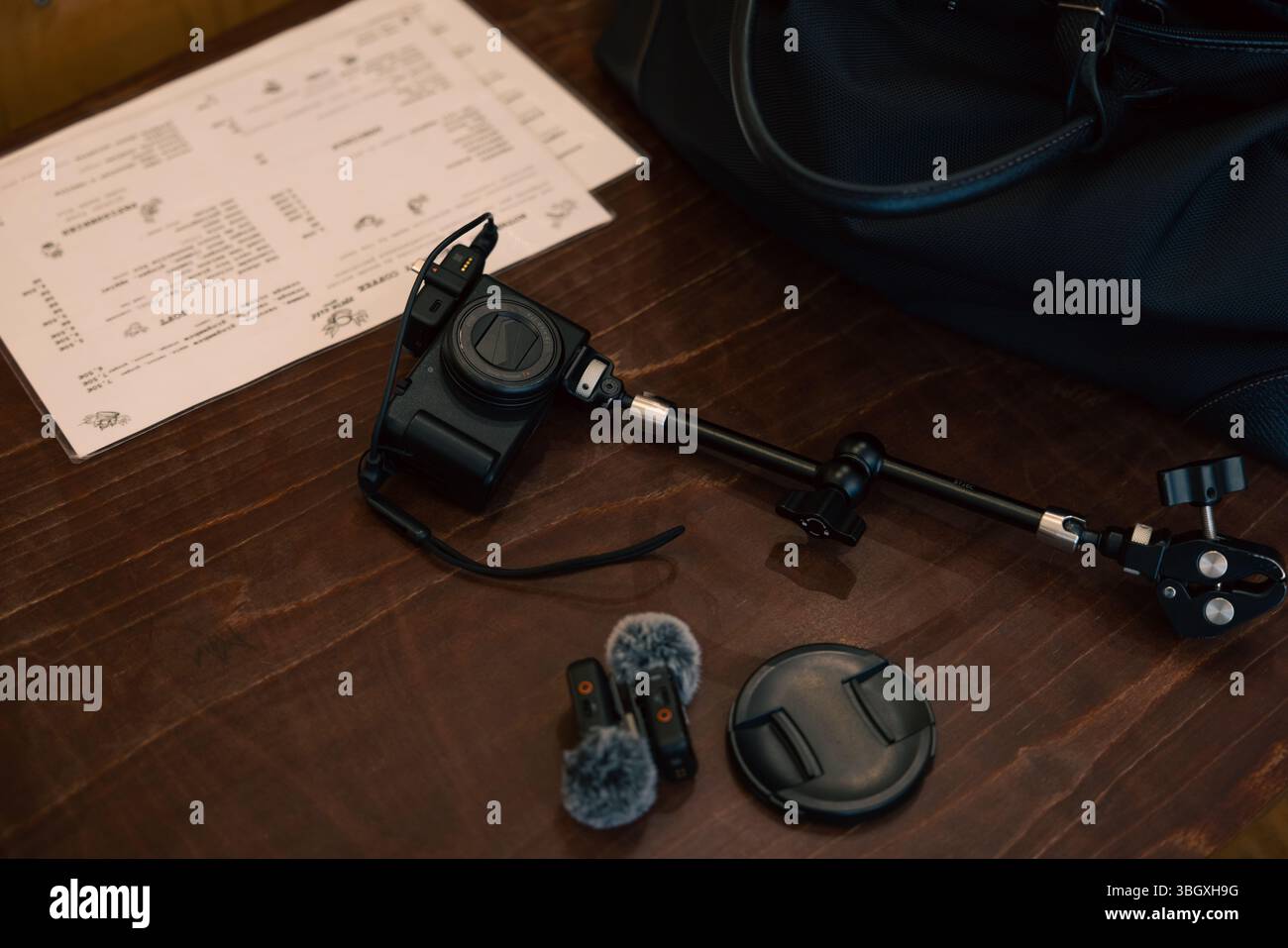 A setup for a vlogger or content creator, featuring a compact camera on a mount with external microphones, laid out on a wooden table. Stock Photo