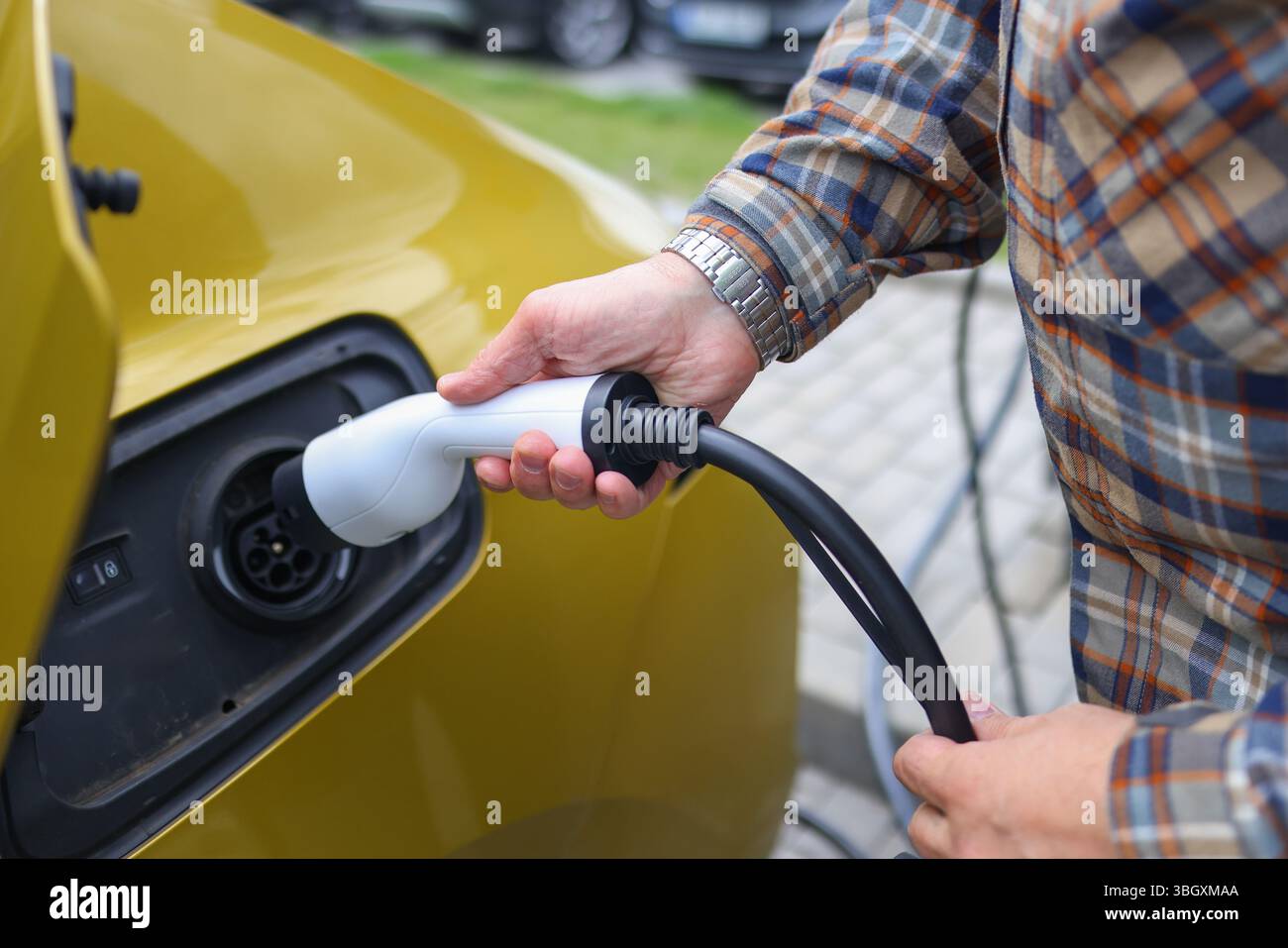 Hand plugging in electric vehicle charger, clean energy and eco transport concept. Stock Photo