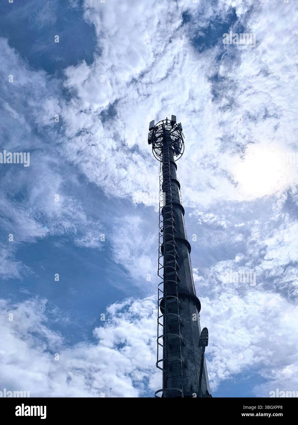 Telecommunication tower stands tall with a backdrop of bright white clouds and a blue sky Stock Photo