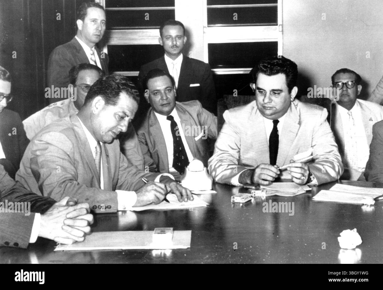 Luis Somoza (right), President of Nicaragua, watches as Panamanian Ambassador to the Organization of American States Ricardo M. Arias Espinoza (left) signs peace documents ending the border dispute between Nicaragua and Honduras. Behind Espinoza, who is head of the OAS fact finding commission, is Brigadier General Anastasia Somoza (stars, half hidden).   10 May 1957 Stock Photo