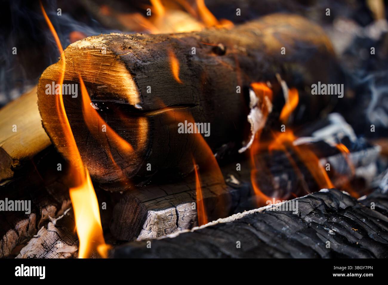 Burning log surrounded by flames in a campfire, close-up view Stock Photo