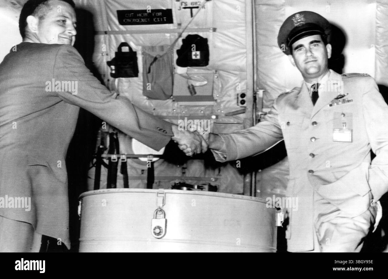 W. H. Orton, Lockheed Missiles and Space Corporation engineer, and USAF Major Richard H. Moore (right) shake hands on a job well done, as the goldplated capsule from Discoverer XXVI (in cannister in foreground) is turned over to the Lockheed representative. 10 July 1961 Stock Photo