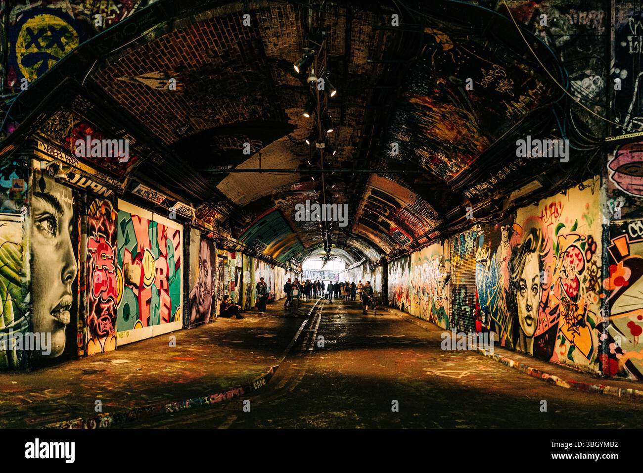 Colorful graffiti-covered tunnel filled with people walking Stock Photo